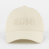 Gorra KUMI en color natural vista de frente, con bordado tono sobre tono de la palabra “KUMI” en pana de algodón orgánico