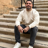 Modelo masculino con la KUMI Natural Unisex Crewneck de algodón orgánico, sentado en escaleras de piedra