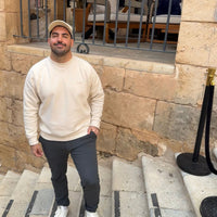 Sudadera KUMI Natural Unisex Crewneck en color natural, fit cómodo, modelo masculino frente a fachada tradicional