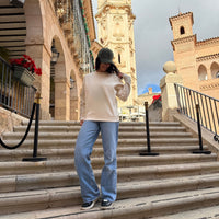 Modelo femenina con la KUMI Natural Unisex Crewneck en color natural, look casual en escaleras con arquitectura mediterránea