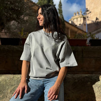 Modelo sonriendo con la OPC Oversize T-Shirt gris de algodón orgánico en entorno mediterráneo