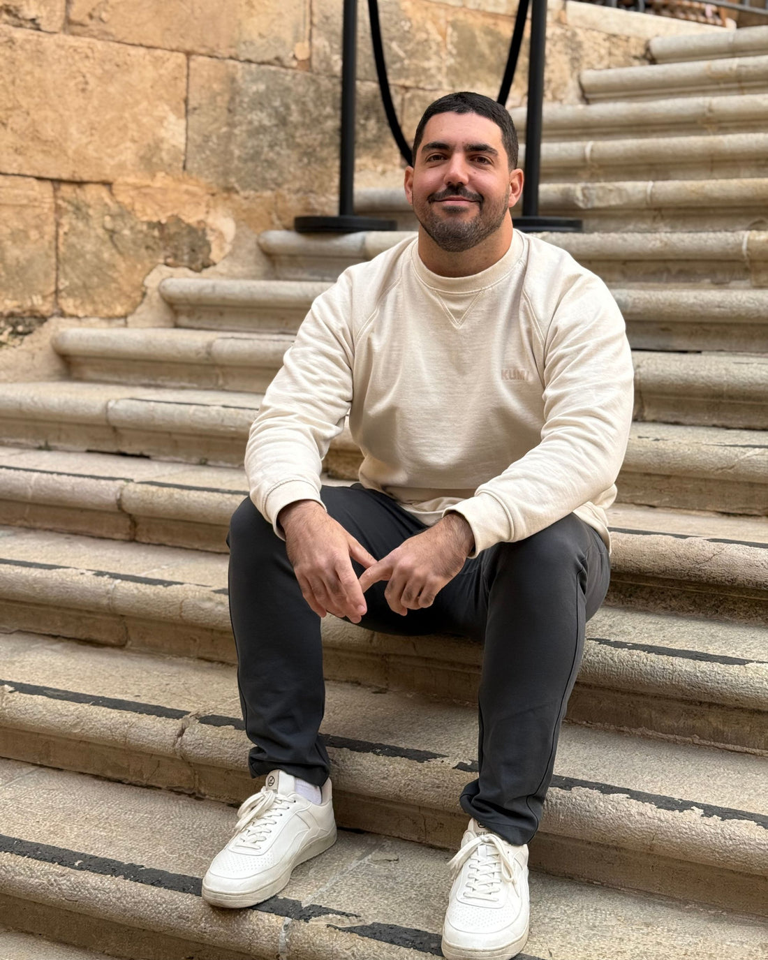 Modelo masculino con la KUMI Natural Unisex Crewneck de algodón orgánico, sentado en escaleras de piedra