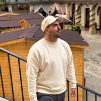 Sudadera KUMI Natural Unisex Crewneck en look casual masculino caminando por entorno urbano mediterráneo