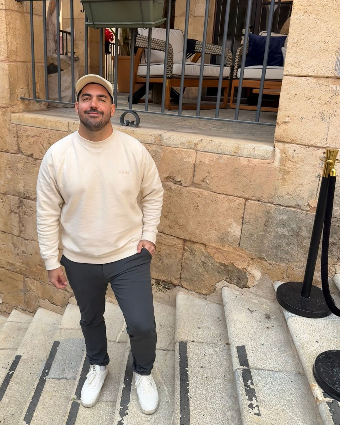 Sudadera KUMI Natural Unisex Crewneck en color natural, fit cómodo, modelo masculino frente a fachada tradicional