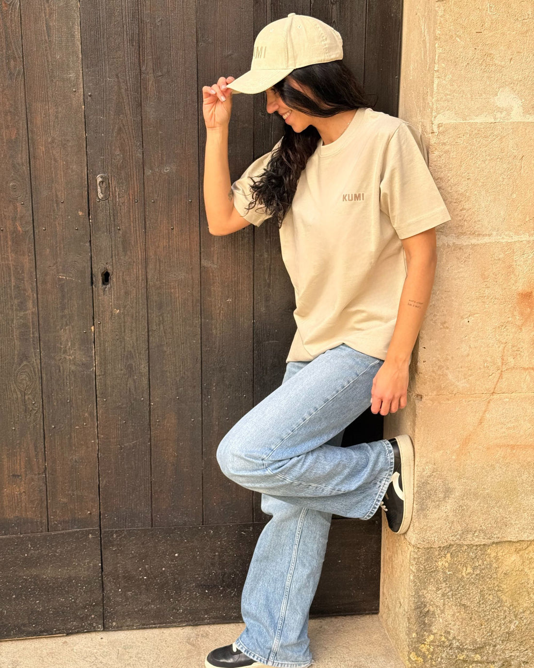 Camiseta KUMI color beige de algodón orgánico, corte regular, en look relajado apoyada en la pared