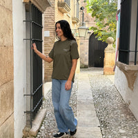 Camiseta KUMI verde oliva de algodón orgánico, corte regular, en look casual caminando por calle empedrada