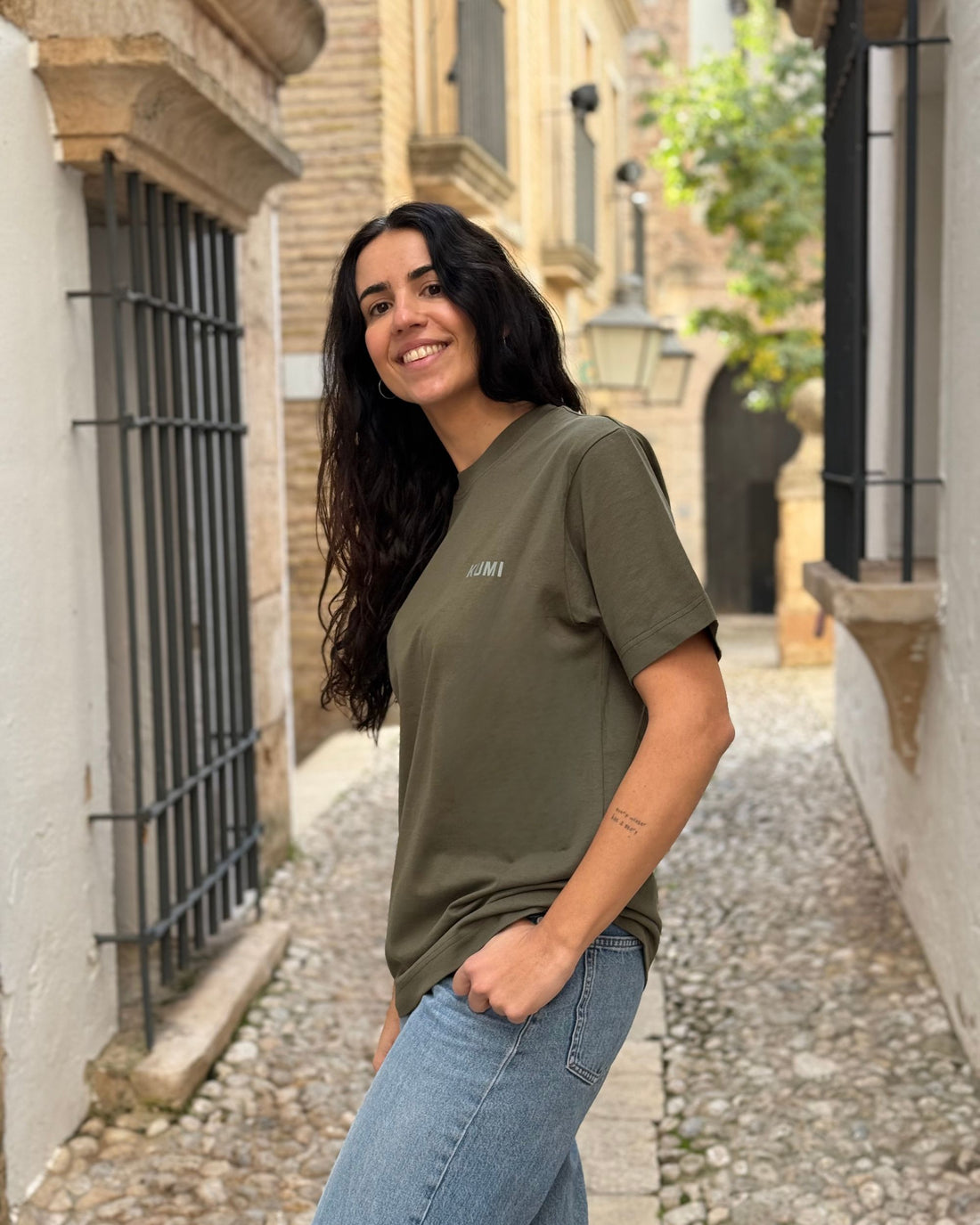 Modelo con Camiseta KUMI verde oliva de algodón orgánico, corte regular, en entorno mediterráneo
