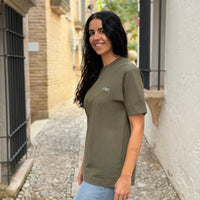 Modelo sonriendo con Camiseta KUMI verde oliva de algodón orgánico, corte regular, en calle empedrada